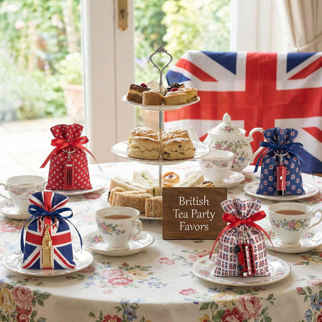 A styled British tea party table setting with teacups, scones on a three-tier stand, and several fabric tea party favors in Union Jack and floral patterns. A wooden sign reads 'British Tea Party Favors' in front of a window with a Union Jack draped backdrop.